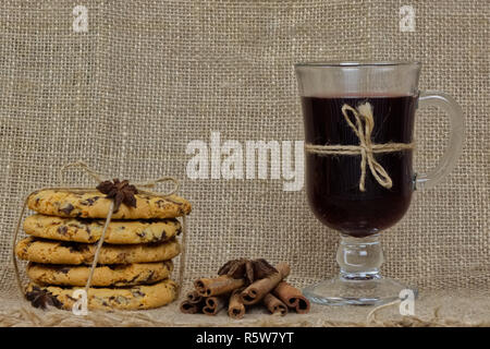Mulled wine with anise. The glass are on a burlap tablecloth surronded by traditional cookies with chocolate and cinnamon sticks. Horizontal photo. Stock Photo