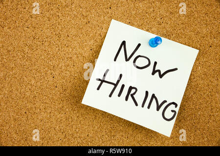 A sticky note on a cork board with the words now hiring on it Stock Photo