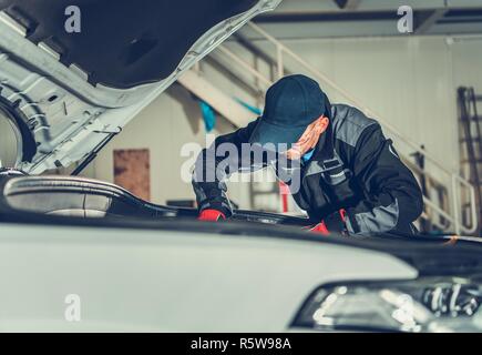 Car Mechanic on Duty. Caucasian Auto Service Worker Looking Under Vehicle Hood For Potential Issues. Automotive Industry. Stock Photo