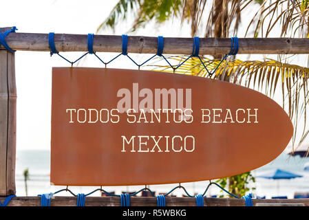 Orange vintage signboard in shape of surfboard with Todos Santos Beach Mexico text for surf spot and palm tree in background Stock Photo