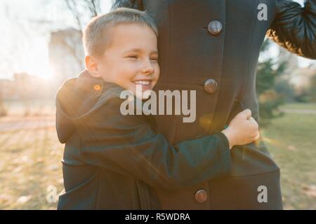 Little son hugging his mother, boy smiling, sunny day in the park, golden hour. Stock Photo
