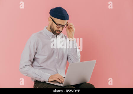 Caucasian male copywriter dressed in stylish clothes, works freelance, types information on laptop computer, connected to wireless internet, has atten Stock Photo
