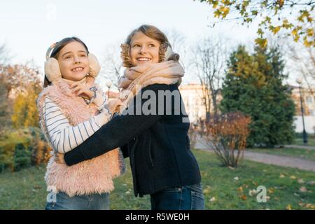 Outdoor portrait of two little girls best friends, smiling girls hugging each other watching the sunset, sunny autumn winter park, golden hour. Stock Photo