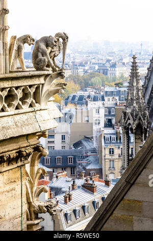 Three stone statues of chimeras overlooking the rooftops of the historic center of Paris from the towers gallery of Notre-Dame cathedral with the city Stock Photo