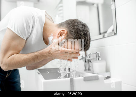 Man washing his face with fresh water and foam in the sink at the white bathroom Stock Photo