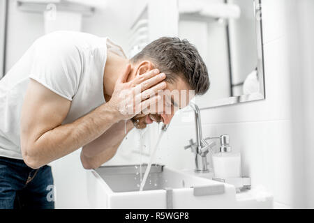 Man washing his face with fresh water and foam in the sink at the white bathroom Stock Photo