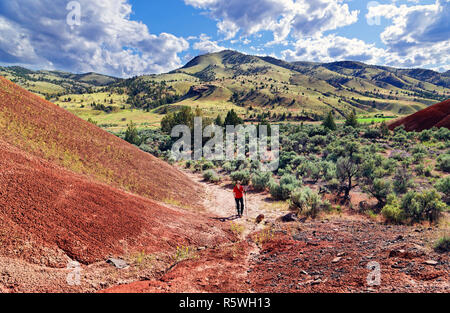 42,887.03094 dry landscape, woman in her 70s hiking a trail in the rolling red sand & sagebrush hills with Juniper trees in the arid Oregon high deser Stock Photo