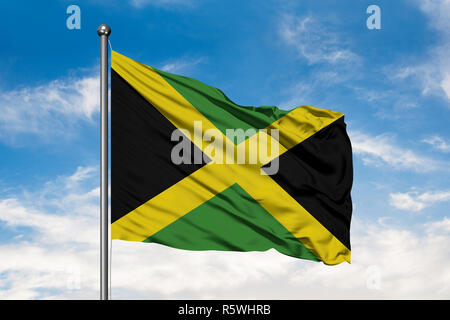 Flag of Jamaica waving in the wind against white cloudy blue sky. Jamaican flag. Stock Photo