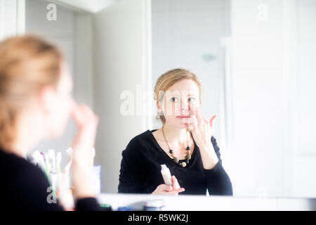Woman standing in bathroom applying make-up Stock Photo