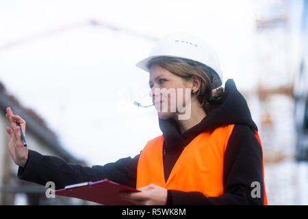 Portrait of a woman in a hard hat holding a clipboard and making a stop gesture Stock Photo