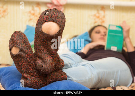 The girl is lying on the couch and is reading a book, in the foreground the holey socks Stock Photo