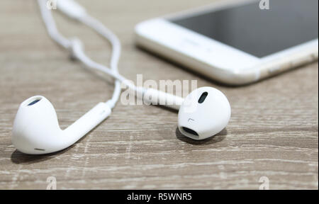White earphones on wooden surface and smartphone in background. Small earbuds close up Stock Photo