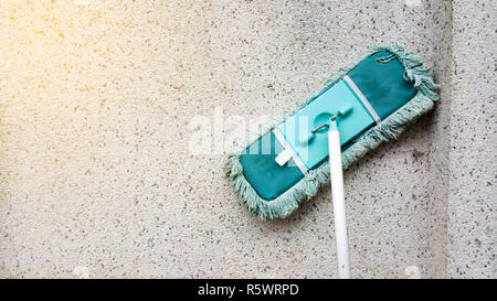 A green dirty mob or swab lean on dirty concrete wall. The floor mop is used to clean the floor clean. Cleaning and exercise by housework concept. Stock Photo