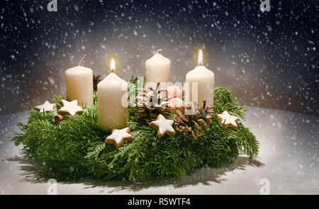 Advent wreath from evergreen branches with white candles, the second is burning for the time before Christmas, dark snowy background with copy space,  Stock Photo