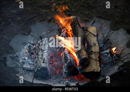 old fire bowl with burning wood logs warms up at an outdoor party in the cold night, copy space, selected focus, narrow depth of field Stock Photo
