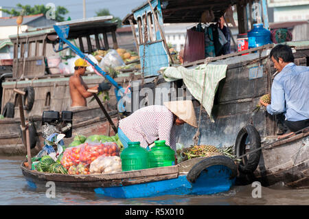 Female boatwoman selling produce hands over a pineapple to a buyer on another wooden boat at the Cai Rang Floating Market, Can Tho Province,Vietnam Stock Photo