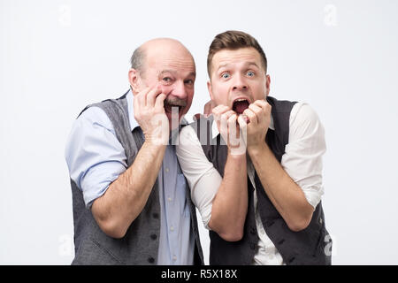 Emotive stupefied men stare at camera with bugged eyes full of fear, keep hands near opened mouthes. Stock Photo