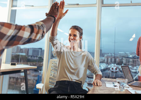 business colleagues giving high five to each other in office. Team members celebrating success at work by giving high five. Stock Photo