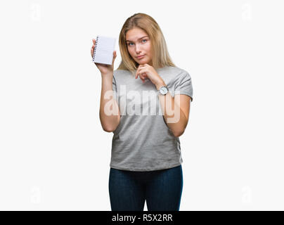 Young caucasian woman holding blank notebook over isolated background serious face thinking about question, very confused idea Stock Photo