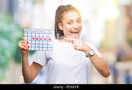 Young braided hair african american girl holding menstruation calendar over isolated background very happy pointing with hand and finger Stock Photo