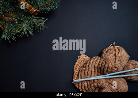 Yarn, knitting needles and basket with pine branches on dark background. Stock Photo
