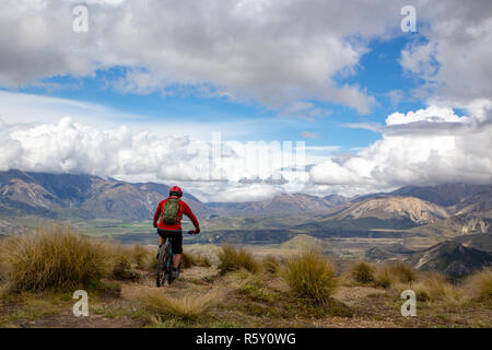 A mountain biker rides along the ridge and descends the mountain with beautiful scenery way down below Stock Photo