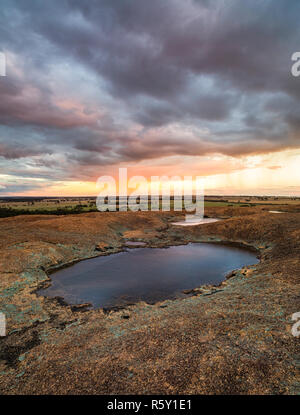 Small pools of water on top of  Hyden Rock (above Wave Rock) with rain falling over the surrounding farmland. Stock Photo