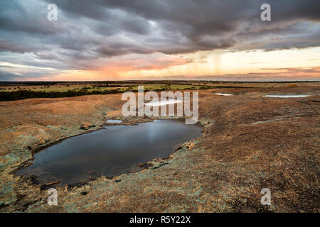 Small pools of water on top of  Hyden Rock (above Wave Rock) with rain falling over the surrounding farmland. Stock Photo