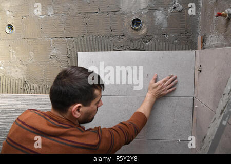 Gluing tiles on the wall. Laying tiles on the wall.  Worker installing big ceramic tiles on the walls Stock Photo