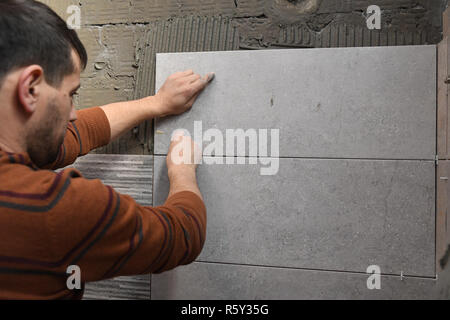 Gluing tiles on the wall. Laying tiles on the wall. Worker installing big ceramic tiles on the walls Stock Photo