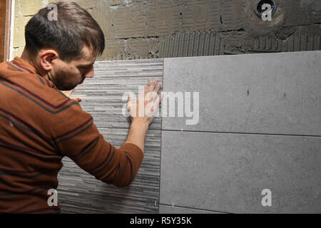 Gluing tiles on the wall. Laying tiles on the wall. Worker installing big ceramic tiles on the walls Stock Photo
