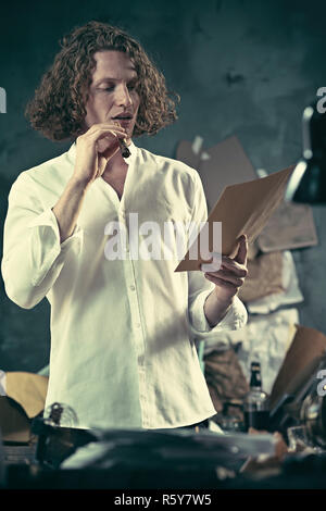 Writer at work. Handsome young writer standing near the table and making up something in his mind Stock Photo