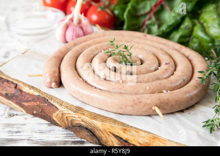 raw sausage for frying Grilled on vintage cutting board With thyme and tomatoes Stock Photo