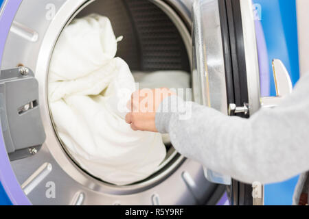 Laundry washing machine. A hand putting or getting some bed sheets from or into the laundry washing machine. Stock Photo