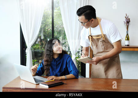 Asian man waitress taking order of woman in the cafe. Cafe restaurant service, Small business owner, food and drink industry concept. Stock Photo