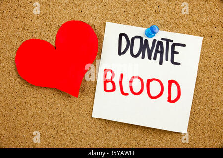 A yellow sticky note writing, caption, inscription Phrase DONATE BLOOD in black ext on a sticky note pinned to a cork notice board Stock Photo