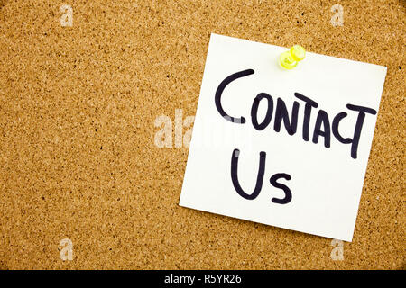 A yellow sticky note writing, caption, inscription Phrase CONTACT US in black ext on a sticky note pinned to a cork notice board Stock Photo