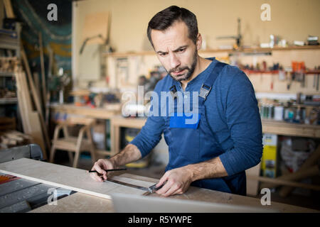 Waist up portrait of frowning carpenter measuring wood while working in joinery, copy space Stock Photo