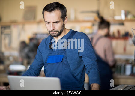 Waist up portrait of mature worker using laptop standing at table in modern workshop, copy space Stock Photo