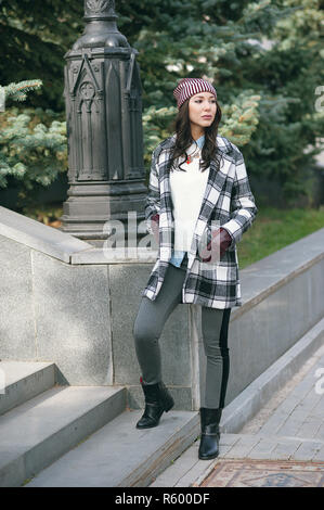 Young beautiful stylish woman, wearing a coat in a white and black cage, white jacket, gray trousers, black boots. Street style, spring and autumn trend, a flirty look Stock Photo