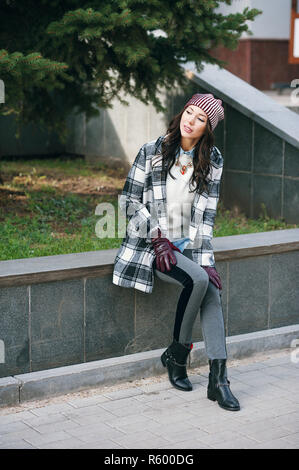 Young beautiful stylish woman, wearing a coat in a white and black cage, white jacket, gray trousers, black boots. Street style, spring and autumn trend, a flirty look Stock Photo