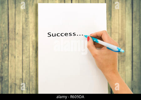 Woman's hand writing word success on white paper sheet, wooden background Stock Photo