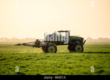 Tractor on the sunset background. Tractor with high wheels is making fertilizer on young wheat. The use of finely dispersed spray chemicals Stock Photo