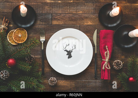 Christmas table setting with empty plate, silverware, burning candles, red table textile on rustic wooden table. Top view, copy space for text. Beauti Stock Photo