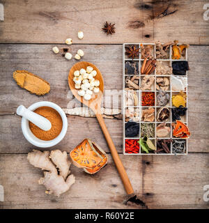 Alternative health care dried various Chinese herbs in wooden box and herbs capsule in wooden spoon with mortar on old wooden background. Stock Photo