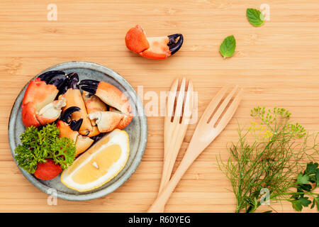 Fresh steamed red crabs leg in bowl . Red crabs leg with ingredients. Steamed red crabs leg with herbs Fennel ,parsley,rosemary,lemon and mint with fork on wooden cutting board. Stock Photo