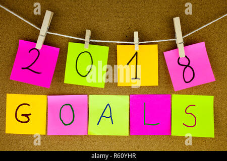 A yellow sticky note post it writing, caption, inscription for goals for 2018 year in black ext on a sticky note pinned to a cork notice board Stock Photo