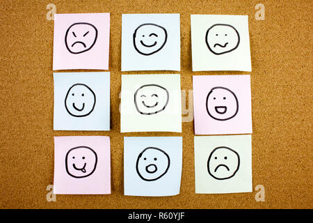 A yellow sticky note post it writing, caption, inscription Crumpled sticky note emoticons smileys in black ext on a sticky note pinned to a cork notice board Stock Photo