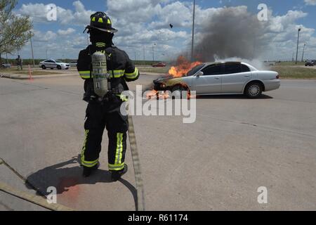 Chunks of concrete explode in to the air from the extreme heat generated by a vehicle fire as William Green, Tinker Fire and Emergency Services firefighter, holds a line-hose moments before spraying water on a vehicle on the fire May 4, 2017, Tinker Air Force Base, Oklahoma. The privately owned vehicle developed mechanical trouble and caught fire near the Oklahoma City Air Logistics Complexs' building 9001. Stock Photo