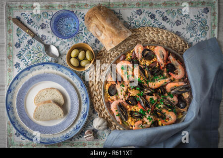 Paella on the metal plate on the beautiful napkin with tableware and bread top view Stock Photo